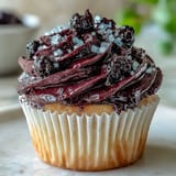 A generous dollop of homemade Black Currant Frosting spreads smoothly over a slice of layer cake.