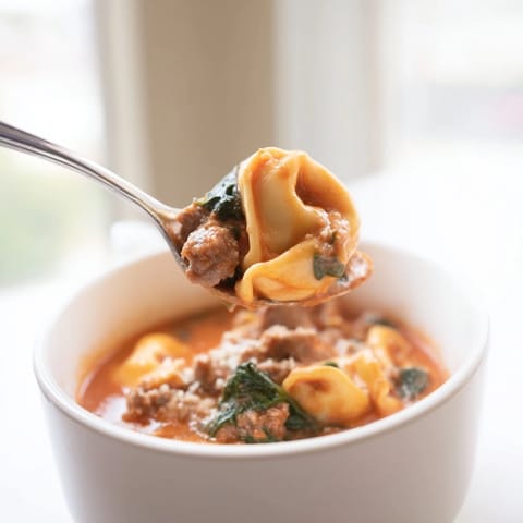 Creamy Tuscan Tortellini Soup with Italian sausage, wilted spinach, and melted Parmesan served in a rustic bowl.  