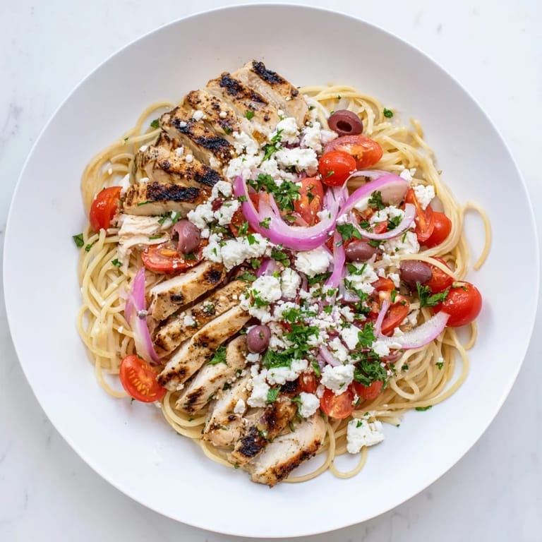 Crumbled feta and fresh parsley garnish this vibrant Mediterranean-inspired pasta dinner on a white plate.